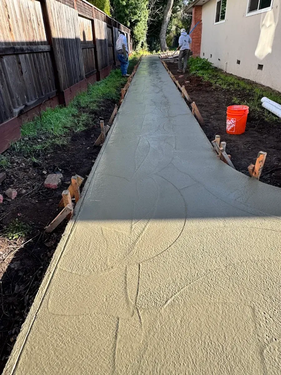 Textured concrete side-yard path beside a fence
